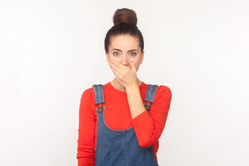 Portrait of attractive shocked surprised woman with hair bun covering mouth with hand, promise to...