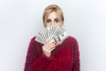 Portrait of shocked surprised young blonde woman standing covering half of face with dollar...