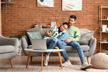 Beautiful young happy couple with laptop resting on sofa at home