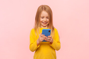 Portrait of smiling joyful blonde little girl holding mobile phone, playing game, watching video,...