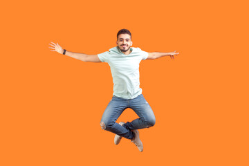 Fototapeta na wymiar Full length portrait of jumping young bearded man wearing T-shirt feeling inspiration rejoicing expressing happiness flying in air. Indoor studio shot isolated on orange background.