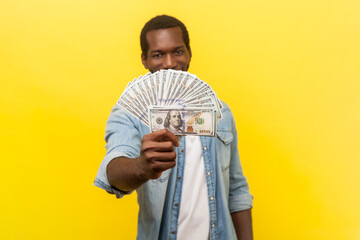 Portrait of satisfied delighted man standing showing dollar banknotes having big salary reward,...