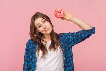 Portrait of confused uncertain brown haired woman holding delicious sugary donut looking at camera...
