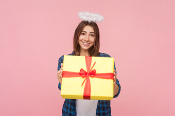 Portrait of cute smiling angelic brown haired woman with nimb over head giving present box, congratulating, offering gift, wearing checkered shirt. Indoor studio shot isolated on pink background. - obrazy, fototapety, plakaty