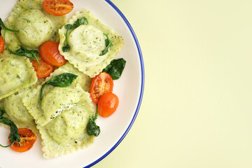 Bowl of tasty ravioli with vegetables on green background