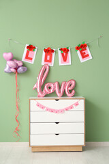Chest of drawers with word LOVE made from balloons and bunting near green wall. Valentine's Day celebration