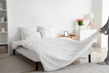 Woman making bed in modern bedroom - obrazy, fototapety, plakaty