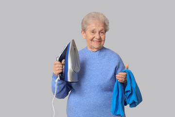 Happy senior woman with iron and  t-shirt on grey background