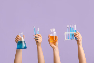 Female hands holding filled flask and bottle with test tubes on lilac background. Chemistry lesson...