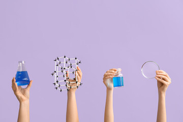 Female hands holding filled flask with bottle, molecular model and Petri dish on lilac background....