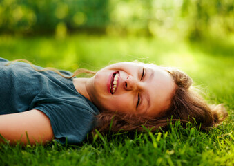 Happy laughing fun casual kid girl lying on the grass on nature summer sunny brigh background. Closeup - 792122887