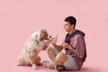 Young man giving high-five to Australian Shepherd dog on pink background