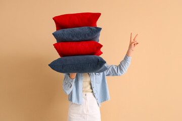 Woman with stack of pillows showing victory gesture on beige background