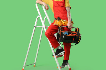 Male electrician on stepladder with tool bag against green background