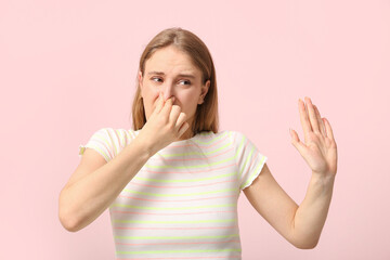 Young woman feeling bad smell on pink background