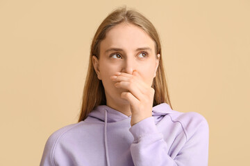 Young woman feeling disgusting smell on beige background