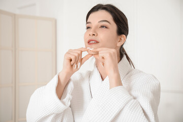 Beautiful young woman in bathrobe doing face building exercise at home