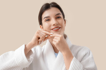 Beautiful young happy woman in bathrobe doing face building exercise on beige background