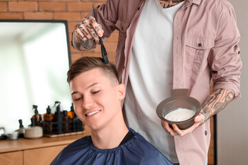 Male hairdresser dyeing client's hair in barbershop, closeup