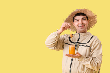 Male beekeeper with honey and spoon on yellow background
