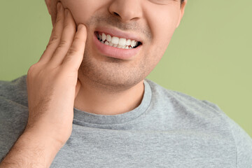 Young man suffering from toothache on green background, closeup