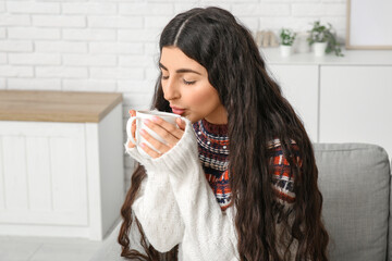 Beautiful young woman drinking hot tea on sofa at home