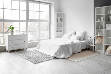 Interior of light bedroom with big bed and shelf units