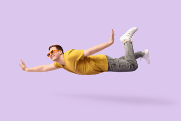 Joyful young man in sunglasses flying on lilac background