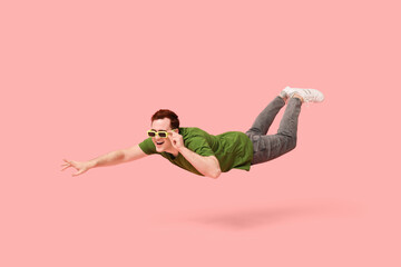 Joyful young man in sunglasses flying on pink background