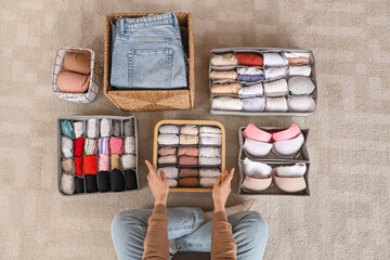 Beautiful young woman with clean clothes in different organizers at wardrobe, top view