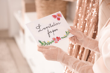 Beautiful young woman holding card with text INVITATION FOR PROM  in wardrobe, closeup