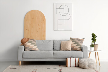 Interior of light living room with grey sofa, pillows, houseplant and picture - obrazy, fototapety, plakaty