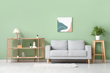 Modern living room with wooden shelving unit and grey sofa near green wall - obrazy, fototapety, plakaty