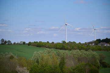 Fototapeta premium Two wind turbines over English countryside against blue sky with small clouds