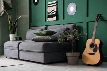 Beautiful interior of green living room with black sofa, coffee table, guitar and houseplants