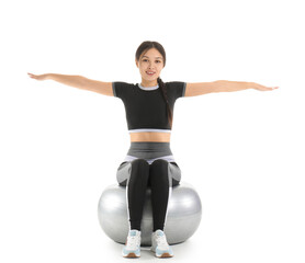 Sporty young Asian woman exercising on fitball against white background