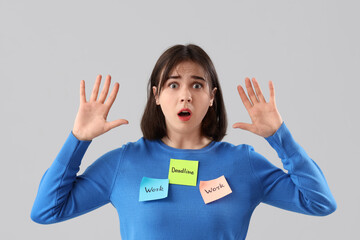 Young stressed woman holding sticky notes with words WORK and DEADLINE on grey background. Stress Awareness Month - obrazy, fototapety, plakaty