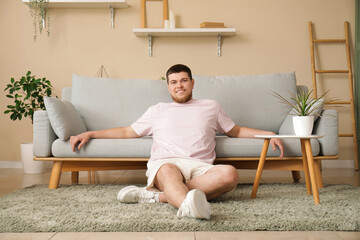 Young man sitting on floor near sofa in living room