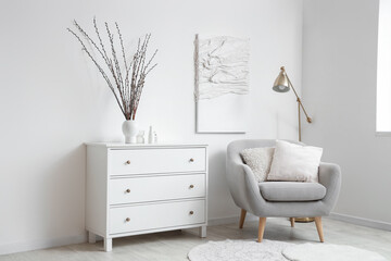 Interior of light living room with armchair, commode and willow branches in vase