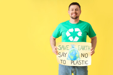 Happy young man in t-shirt with recycling logo holding poster with text SAVE EARTH SAY NO TO...