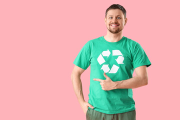 Happy young man in t-shirt with recycling logo pointing at something on pink background. Ecology...