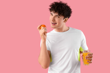 Handsome young happy sporty man with glass of juice and orange on pink background. Weight loss...