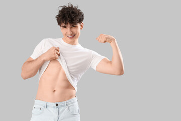 Handsome young happy sporty man showing muscles on grey background. Weight loss concept