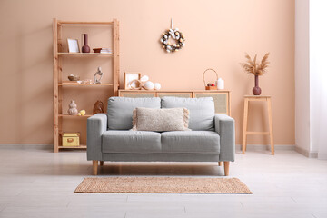 Sofa, shelving unit and Easter wreath decorated with eggs on beige wall in living room