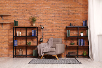Shelving units, grey armchair and lamp near brown brick wall in living room