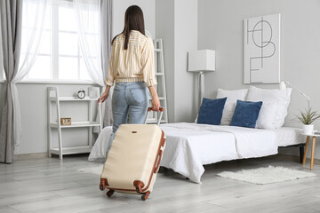 Woman with suitcase in light hotel room, back view