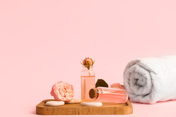 Bottles of cosmetic oil, roses, spa stones and wooden tray on pink background