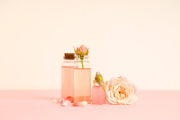 Composition with bottles of cosmetic oil, petals and roses on pink background