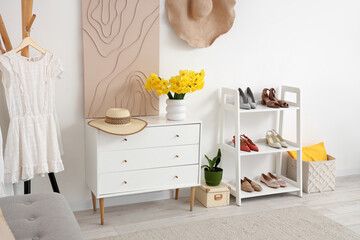 Stylish interior of modern hall with chest of drawers, daffodil flowers and shelving unit