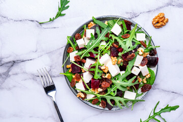 Sweet beetroot salad with feta cheese, fresh arugula, raisins and nuts, marble table background, top view - 792153298